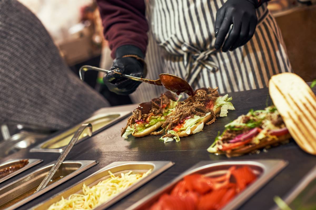 A chef preparing a sandwich with fresh salad. Food cort of street fair. Kitchen outdoors