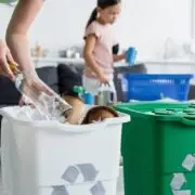 Woman holding bottle near trash can with recycle sign at home