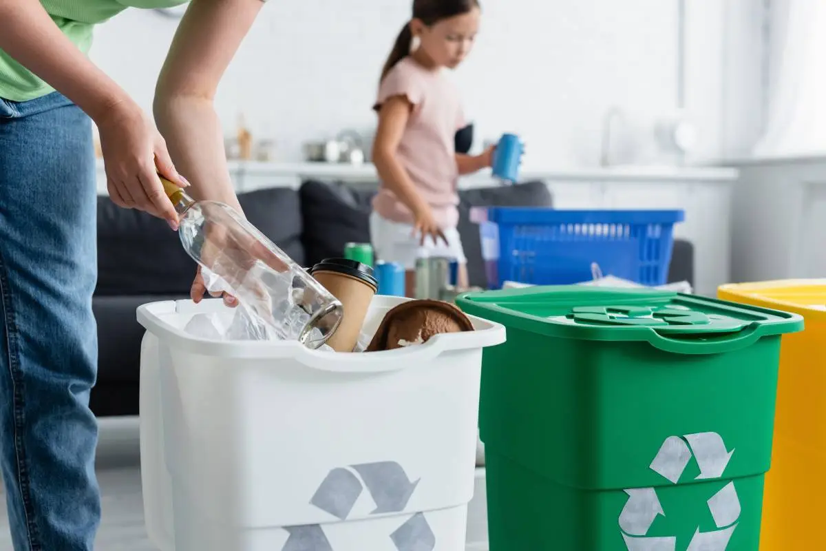 Woman holding bottle near trash can with recycle sign at home